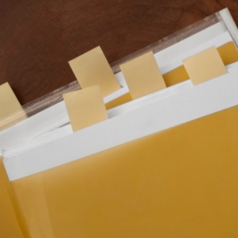 Varias carpetas amarillas con etiquetas blancas y notas adhesivas que sobresalen de la parte superior, colocadas sobre una superficie de madera.